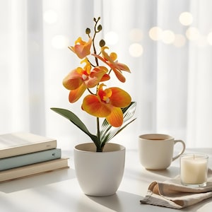 May include: A faux orchid plant with vibrant orange and yellow blooms, set in a white ceramic pot. A white mug, a candle in a glass, and a stack of books are on a white surface, creating a serene scene.