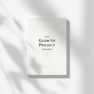 Könnte beinhalten: Ein weißes Notizbuch mit dem Titel "THE GLOW UP PROJECT" und dem Untertitel "Weekly Reset". Das Notizbuch liegt auf einer weißen Oberfläche, wobei Schatten von Blättern eine natürliche Ästhetik erzeugen.