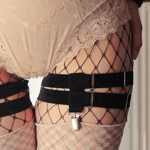 May include: Black fishnet stockings with a black garter belt and silver clips. The garter belt has two straps.