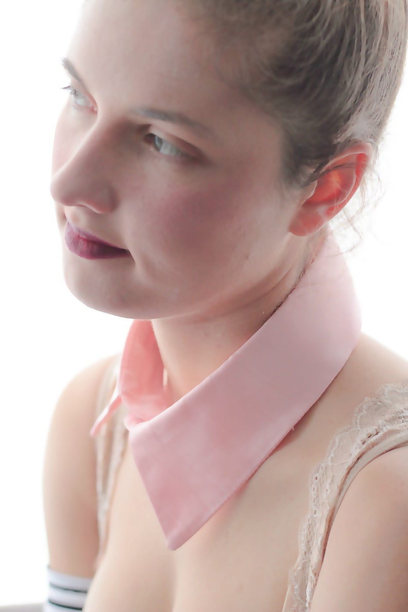 May include: A woman with a pink collar and a lace-trimmed top. The collar is a simple, wide, and flat design.