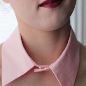May include: A pink fabric collar with a button closure. The collar is worn over a white lace top.