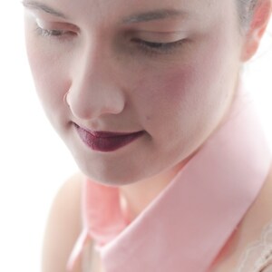 May include: A woman with a pink collar and dark lipstick looks down. Her skin is fair and she has a nose ring.
