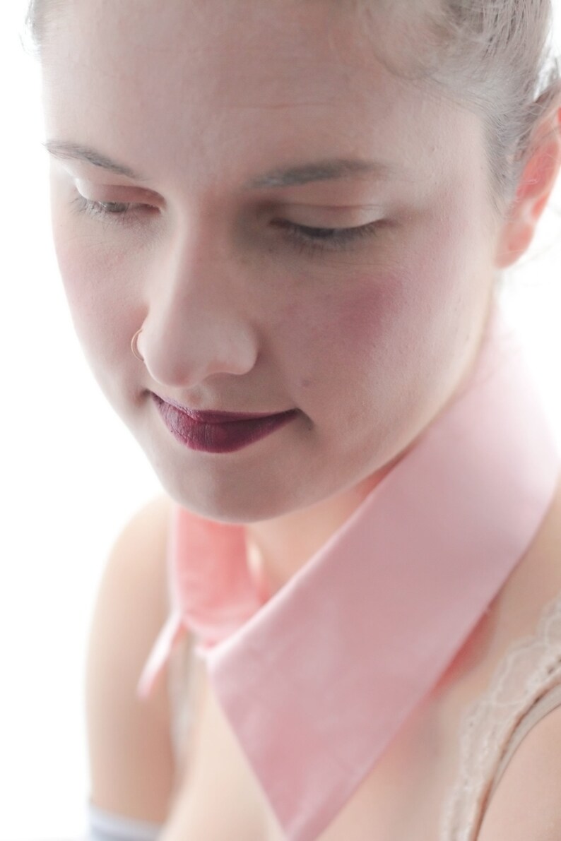 May include: A woman with a pink collar and dark lipstick looks down. Her skin is fair and she has a nose ring.