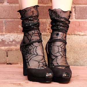 Puede incluir: Zapatos de tacón negros con plataforma y puntera abierta con calcetines negros transparentes con un diseño de telaraña brillante. Los calcetines están fruncidos en el tobillo. Los tacones tienen un tacón de aguja alto y una suela de plataforma.