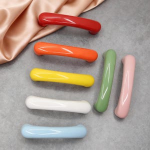 Peut inclure: Ensemble de poignées de meubles colorées, comprenant des teintes de rouge, orange, jaune, blanc, vert, rose et bleu. Ces poignées en céramique présentent une finition brillante et une forme incurvée, parfaites pour égayer tout meuble.