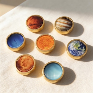 May include: A collection of seven round, brass-rimmed decorative objects, each featuring a different planet or celestial body. The designs include Earth, Mars, Jupiter, the Sun, and other planets, with vibrant colors and detailed imagery.