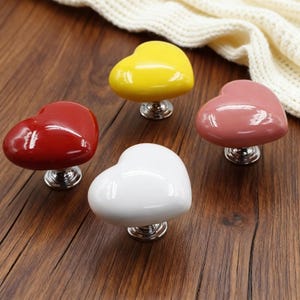 May include: A white ceramic mug with a black handle and the text "But First, Coffee" in a bold, black font. The mug is filled with a dark liquid, likely coffee, and sits on a light-colored surface.