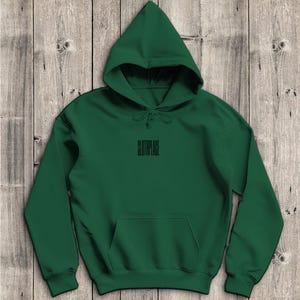Könnte beinhalten: Ein dunkelgrüner Kapuzenpullover mit Kordelzugkapuze und Vordertasche. Das Wort "SLOTHPLACE" ist schwarz auf der Brust zentriert aufgedruckt. Der Kapuzenpullover ist aus weichem Material.