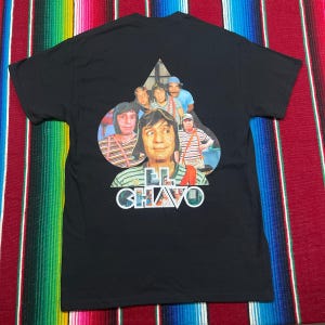May include: Black t-shirt with a colourful graphic of characters from the television show "El Chavo del Ocho." The graphic includes the text "El Chavo" in white and green. The shirt is made of a soft material.