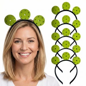 May include: A woman wearing a black headband with three green pickleballs attached. Several similar headbands with pickleball accents are displayed on a white background. The pickleballs are a bright green color and have multiple holes.