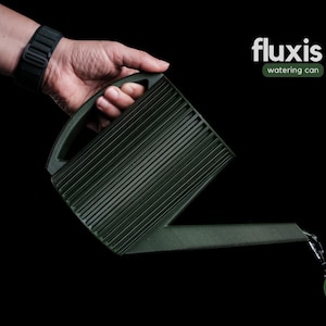 May include: A dark green watering can with a ribbed design is held against a black background. The can is pouring water. The text "fluxis watering can" is displayed in white and green. The design company's logo is also visible.