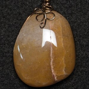May include: A polished, teardrop-shaped pendant with a warm, golden-yellow hue. The stone is accented with a delicate, wire-wrapped bail in a bronze tone. The pendant is a unique piece of jewelry.