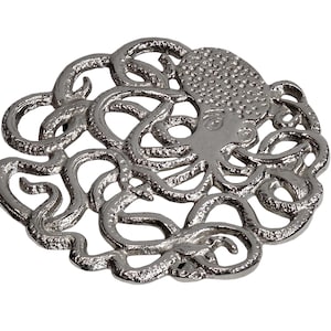 May include: A silver-colored octopus-shaped decorative object. The octopus has a textured head and detailed tentacles that form a circular design. The object is likely made of metal and is set against a white background.