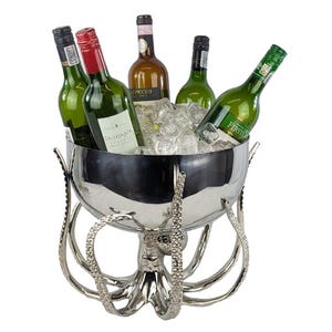May include: A polished silver-toned metal beverage cooler shaped like an octopus with eight curved tentacles forming the base. The bowl is filled with clear ice cubes and contains five glass wine bottles with various labels and coloured caps.