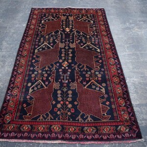 Puede incluir: Alfombra rectangular con un campo azul oscuro y un patrón geométrico detallado en tonos rojos y marrones. La alfombra presenta un diseño central con motivos simétricos y un borde decorativo.