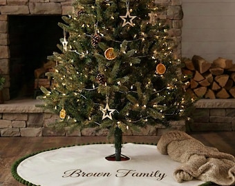 May include: A decorated Christmas tree with star ornaments, pine cones, and orange slices. The tree skirt is white with a green pom-pom trim and the words "Brown Family". A cozy blanket rests nearby.