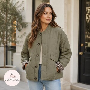 Puede incluir: Chaqueta acolchada verde oliva con cuello redondo y cierre de botones. La chaqueta tiene dos bolsillos delanteros y puños con estampado de leopardo. La chaqueta se usa con jeans azules.