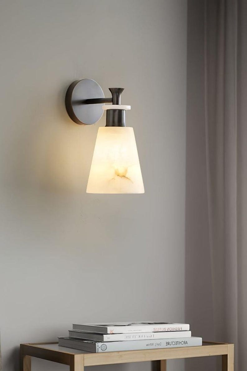 Puede incluir: Aplique de pared moderno con acabado met&aacute;lico oscuro y pantalla c&oacute;nica blanquecina. La pantalla tiene un aspecto veteado y la luz es c&aacute;lida. El aplique est&aacute; montado en una pared gris, dise&ntilde;o minimalista.