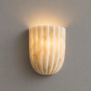 May include: A semi-circular wall sconce crafted from off-white stone with a natural veined pattern. The fixture features a vertical fluted design that diffuses a warm, soft glow from within, creating an illuminated effect across the surface.