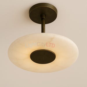 May include: A contemporary ceiling light fitting featuring a circular, off-white shade and a dark bronze metal base. The light has a disc-shaped shade with a dark centre and a matching circular base that attaches to the ceiling. The fitting is designed for indoor use.