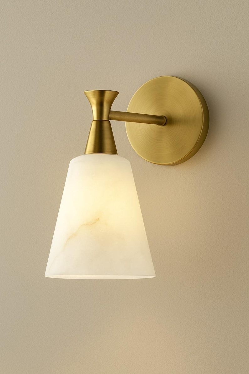 Puede incluir: Aplique de pared con acabado de lat&oacute;n y una pantalla blanca en forma de cono. La pantalla tiene un aspecto veteado. El aplique est&aacute; fijado a una base redonda de lat&oacute;n. Esta luminaria est&aacute; dise&ntilde;ada para iluminaci&oacute;n interior.
