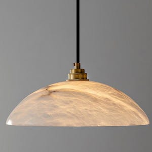 May include: A dome-shaped pendant light featuring a translucent, marbled white stone shade with subtle grey veining. The fixture includes a brass-toned metal cap at the top, connected to a thin, straight black cord that extends upward from the center.