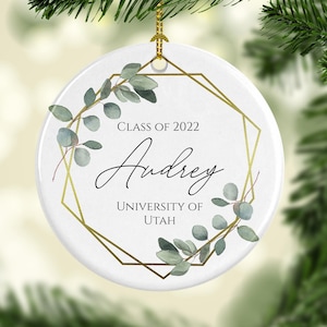 May include: White ceramic ornament with a gold geometric frame and green eucalyptus leaves. The ornament reads "Class of 2022 Audrey University of Utah".