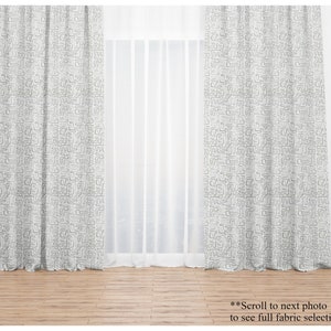 May include: Two light gray patterned curtains with a geometric design hang in front of a sheer white curtain. The image also shows a selection of fabric patterns in shades of gray and white. The text at the bottom says "Scroll to next photo to see full fabric selection."