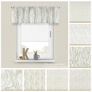 May include: A beige valance with a white abstract pattern. The valance is hung on a window with a white frame. The window is in a room with a light beige wall. The image also shows a variety of fabric swatches with different patterns in beige and white.