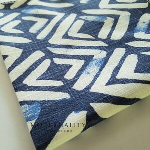 May include: A folded piece of fabric with a white and blue geometric pattern. The fabric has a textured surface and is folded in half. The text "MODERNALITY HOME DECOR" is visible on the fabric.