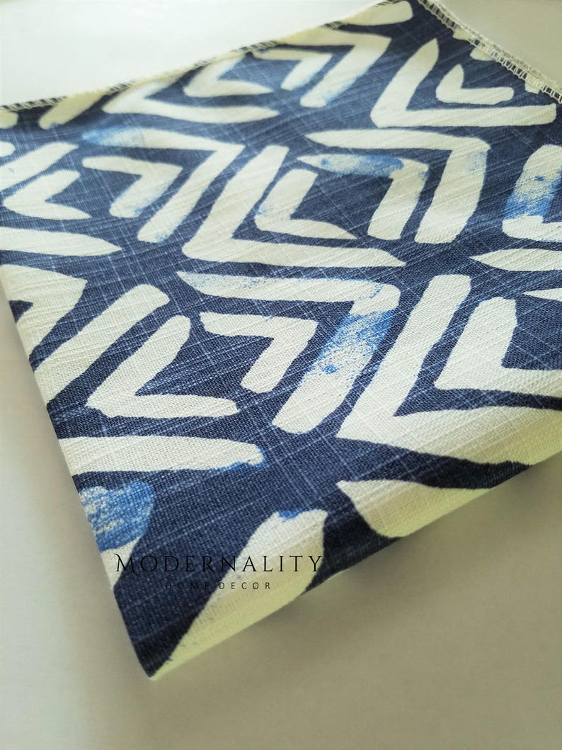 May include: A folded piece of fabric with a white and blue geometric pattern. The fabric has a textured surface and is folded in half. The text "MODERNALITY HOME DECOR" is visible on the fabric.