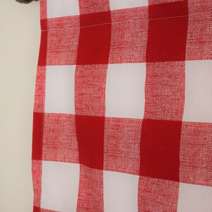 May include: Red and white checkered curtain panel with a white background and red squares. The curtain is hung on a silver curtain rod.