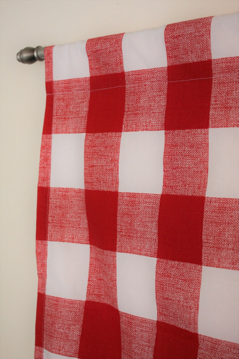 May include: Red and white checkered curtain panel with a white background and red squares. The curtain is hung on a silver curtain rod.