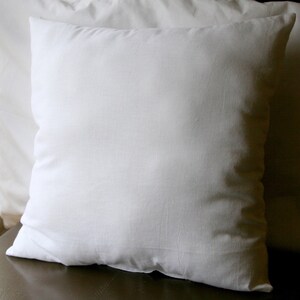 May include: A white pillow with a smooth, plain surface. The pillow is lying on a brown surface.