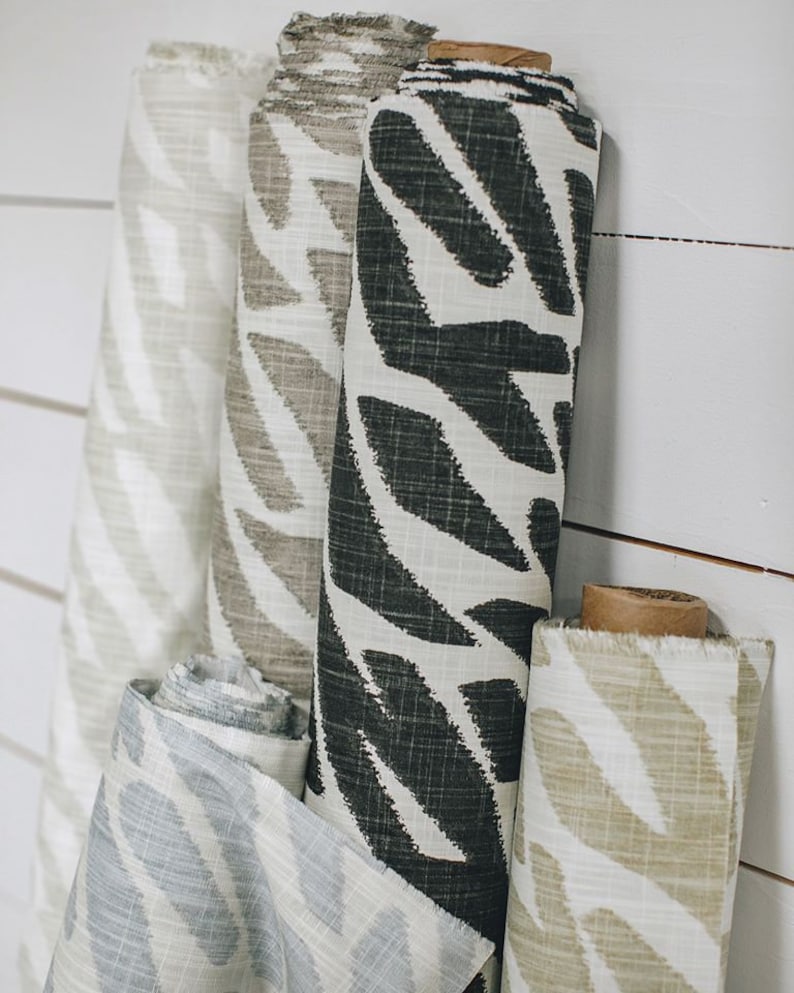 May include: Four rolls of fabric with a white background and a black and white leaf pattern. The fabric rolls are arranged vertically and are hanging on a white wall.