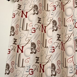 May include: Curtains with a cream background and a pattern of letters in red, brown, and grey. The letters are stylised and include the letters A, B, G, N, R, S, U, and Z.
