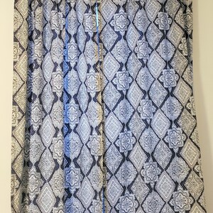 Puede incluir: Un par de cortinas de color azul y blanco con un dise&ntilde;o geom&eacute;trico. Las cortinas est&aacute;n colgadas en una pared blanca.