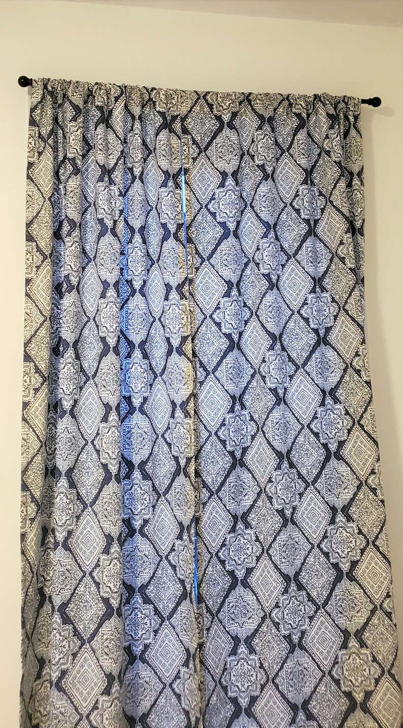 Puede incluir: Un par de cortinas de color azul y blanco con un dise&ntilde;o geom&eacute;trico. Las cortinas est&aacute;n colgadas en una pared blanca.