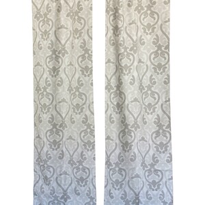 May include: A pair of white and grey patterned curtains with a damask design. The curtains are hanging from a black rod. The text "MODERNALITY HOME DECOR" is printed on the bottom right corner of the curtains.