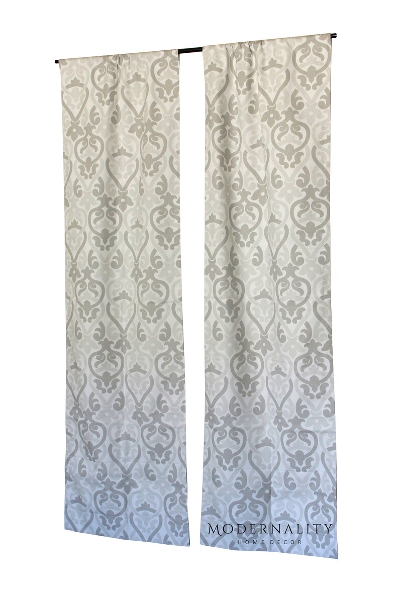 May include: A pair of white and grey patterned curtains with a damask design. The curtains are hanging from a black rod. The text "MODERNALITY HOME DECOR" is printed on the bottom right corner of the curtains.