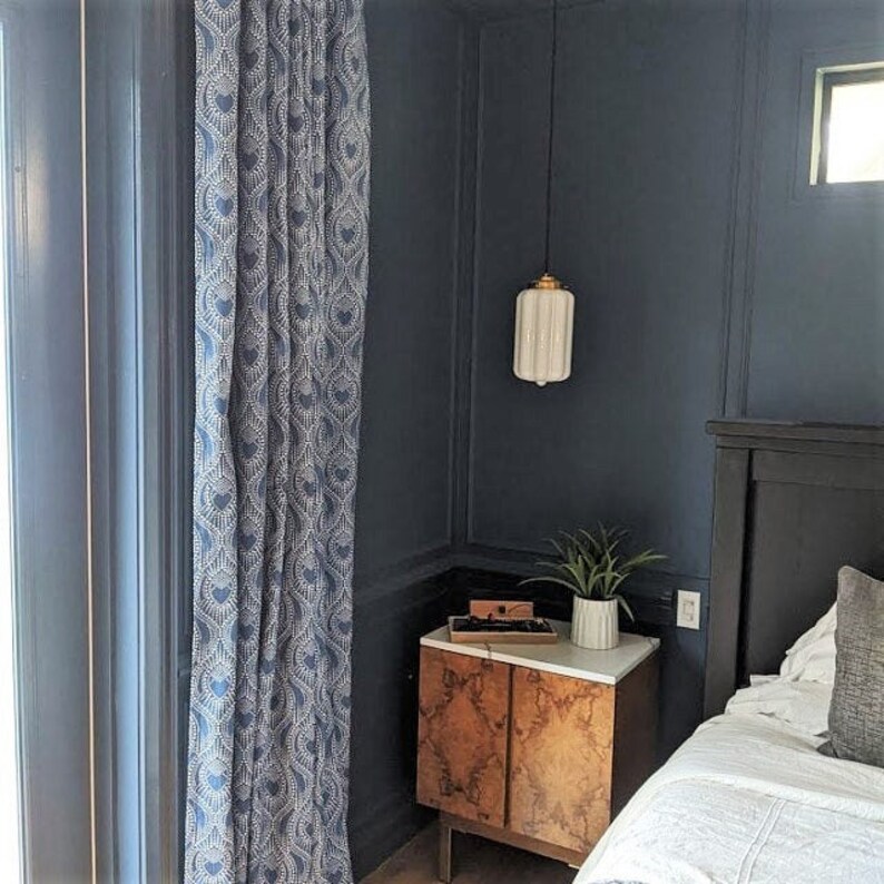 May include: A bedroom with a dark blue wall, a white pendant light, a nightstand with a wooden top and two drawers, and a bed with white bedding and a gray throw pillow.