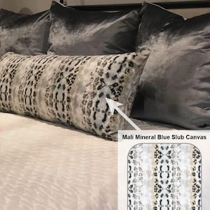 May include: A long, rectangular throw pillow with a white, gray, and black abstract animal print pattern. The pillow is on a bed with gray velvet pillows. The text "Mali Mineral Blue Slub Canvas" is visible below the pillow.