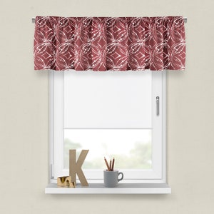 May include: A red valance with a white geometric pattern. The valance is hung on a white window with a white window sill. There is a wooden letter K, pencils in a gray cup, and a gold ring on the window sill.