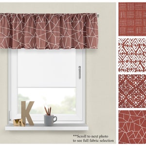 May include: A red and white geometric patterned valance with a white window frame and a white window sill. The window sill has a gold letter K and a small cup with pencils.