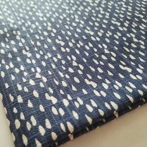 May include: A close-up of a blue fabric with a white polka dot pattern. The fabric has a subtle texture and is folded over on itself.
