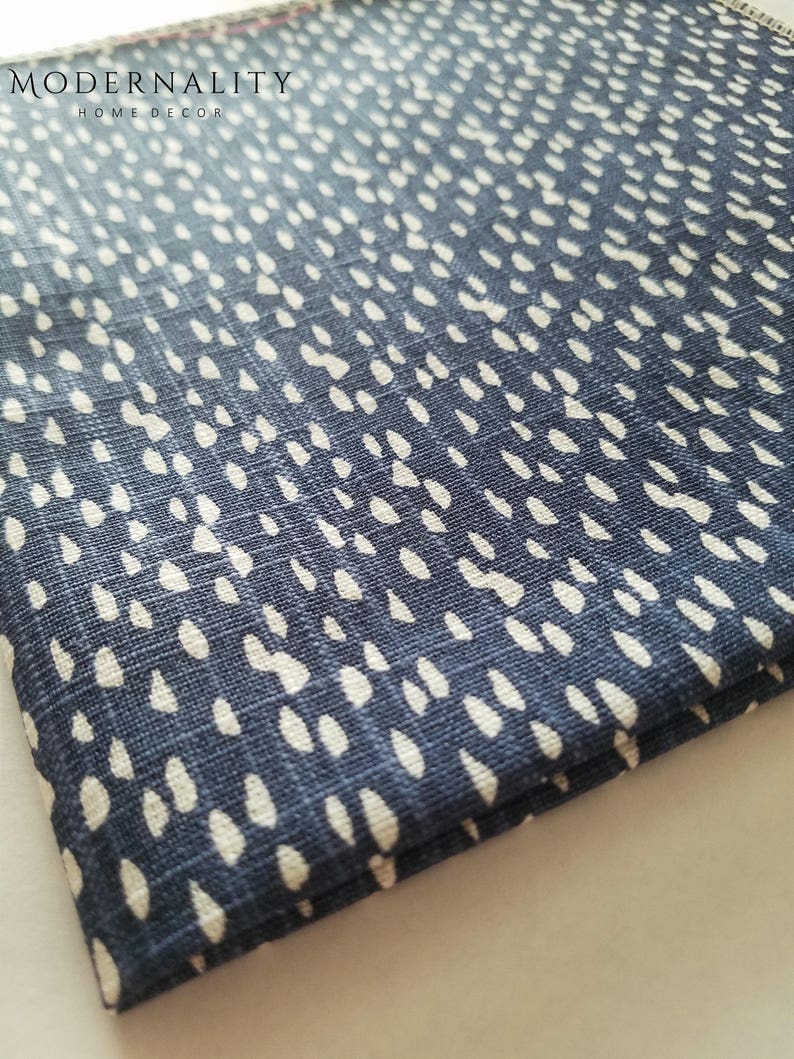 May include: A close-up of a blue fabric with a white polka dot pattern. The fabric has a subtle texture and is folded over on itself.