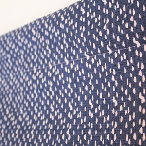 May include: A close-up of a blue fabric with a white polka dot pattern. The fabric is hanging from a curtain rod.