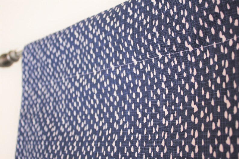 May include: A close-up of a blue fabric with a white polka dot pattern. The fabric is hanging from a curtain rod.