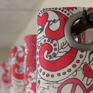 May include: Close-up of a red and white patterned curtain with a silver grommet and a black curtain rod. The curtain has a peace sign and hearts printed on it.
