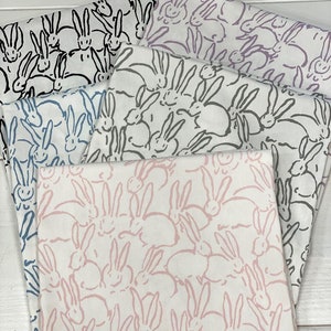 May include: Four fabric swatches with a white background and a repeating pattern of pink, black and blue bunnies. The bunnies are drawn in a simple, stylised way.